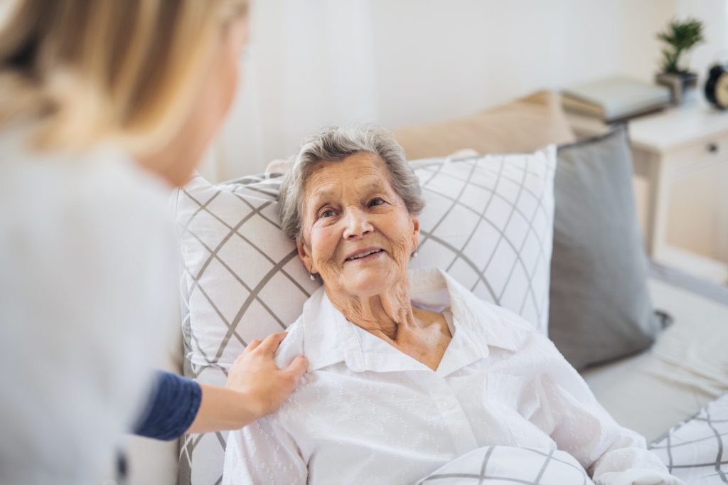 A health visitor talking to a sick senior woman lying in bed at home.