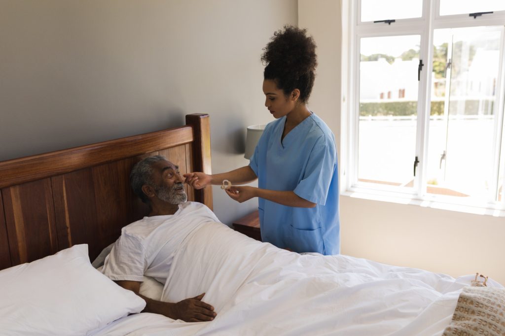 Woman doctor fitting a senior man with hearing aid in bed